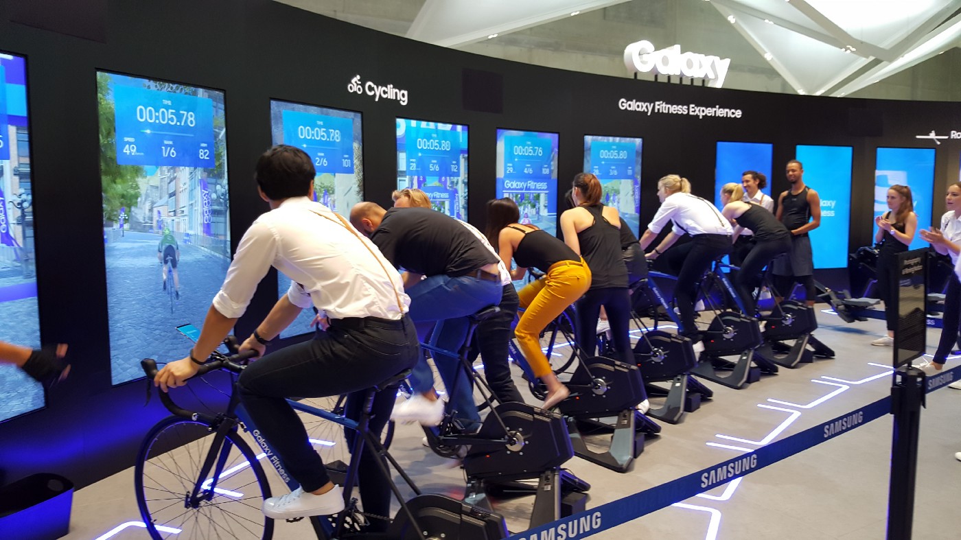 People using exercise bikes in front of big screens